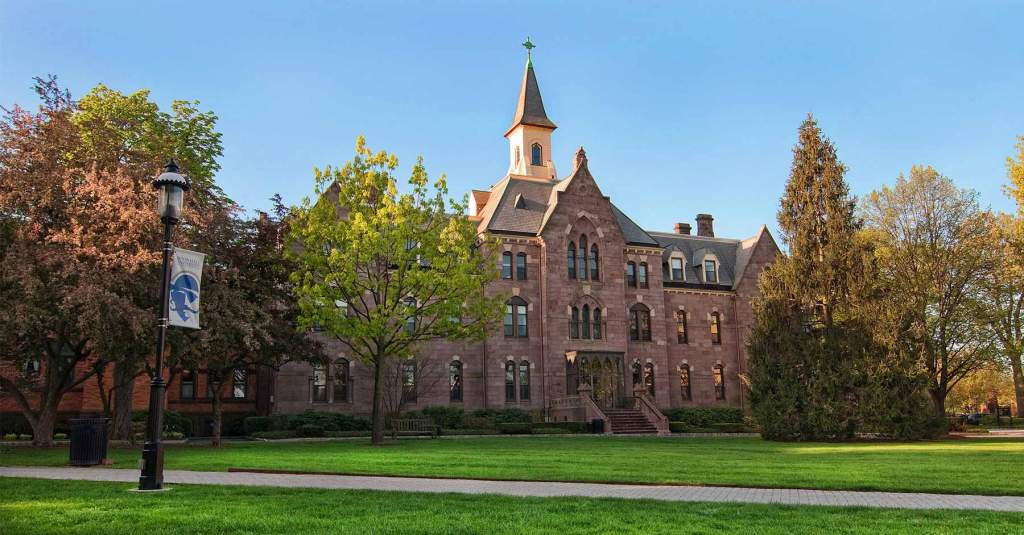 A photo of President's Hall on the campus Green of Seton Hall University. A lamppost is in the lefthand corder with a Pirate banner.